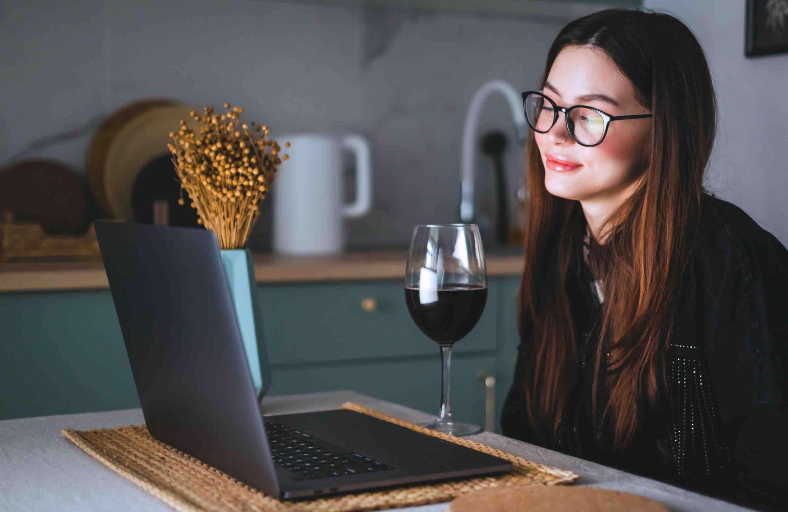 Woman in kitchen on zoom call on laptop with a glass of wine for a blog about virtual networking ideas