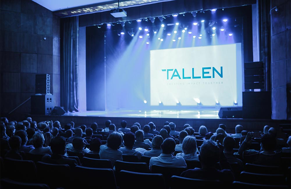 Audience attending a live event production with stage lighting, video, and scenic elements.
