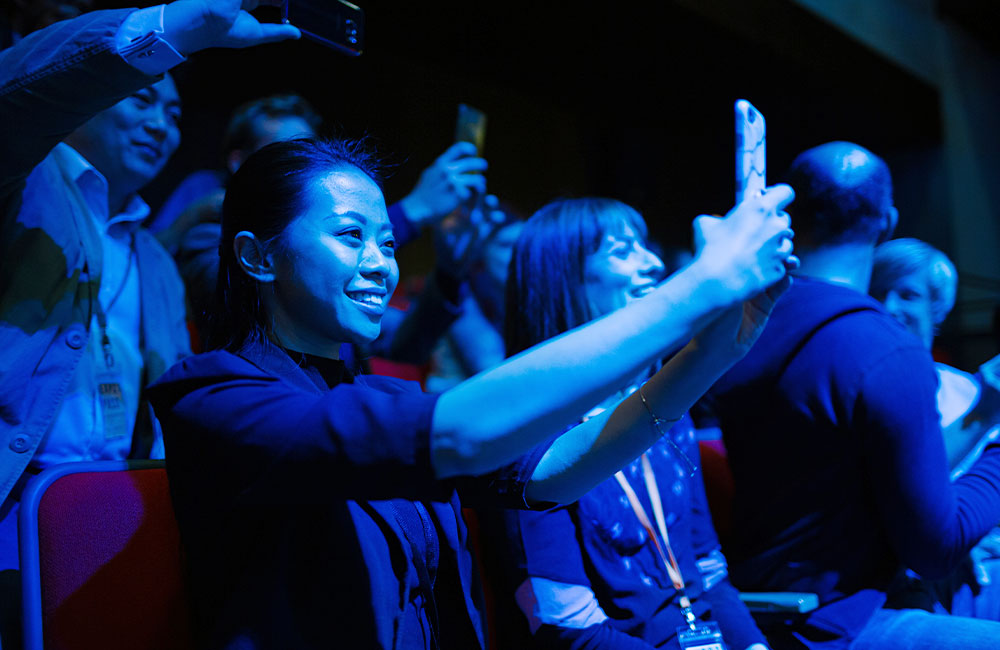 Woman holding up her phone in crowd for a blog about in-person event strategy